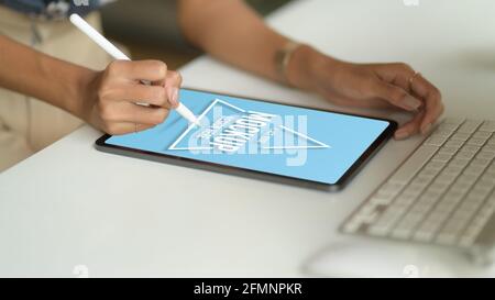 Cropped shot of female hand drawing on mock up tablet with stylus on computer table in office room Stock Photo