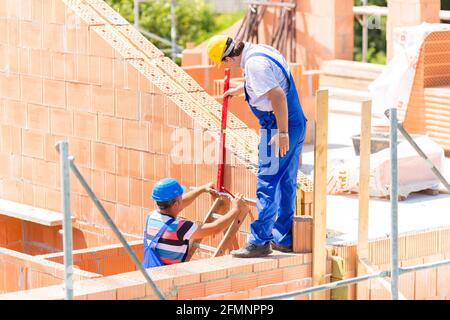 Two builder or worker with helmets controlling walls in scaffold with a bubble level on building or construction site Stock Photo