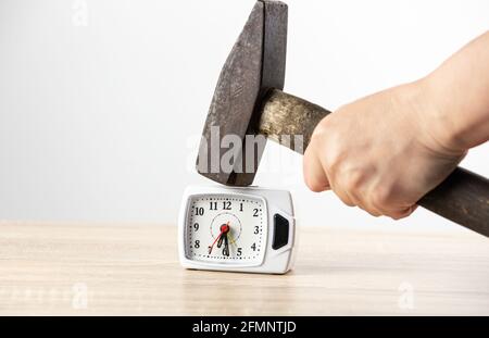 Close up view of person hand holding hammer and smashing alarm clock. Anger management and hating mornings concept. Stock Photo