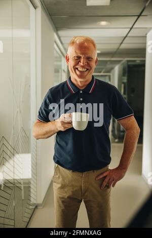 Happy senior businessman having coffee. Male executive having a coffee break at office. Stock Photo