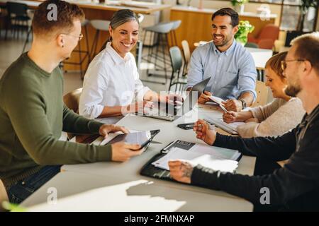 Man sitting in meeting and sharing work details with colleagues. Happy creative team sitting with manager in meeting discussing new project. Stock Photo