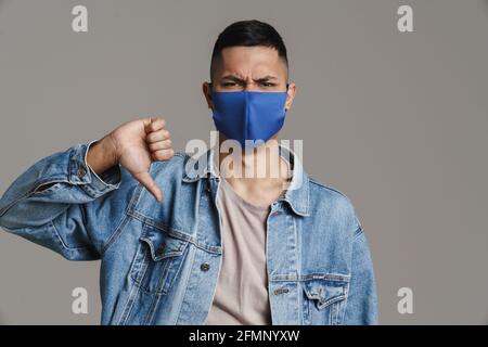Displeased guy in medicine protective mask showing thumb down isolated over grey background Stock Photo