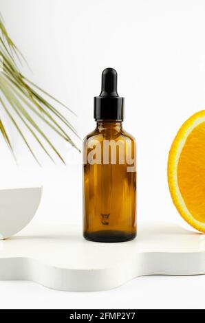 Serum in a glass bottle with a pipette. Natural essential oil on a white podium. Packaging for a cosmetic product. Oils with orange extract Stock Photo
