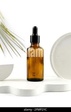 Serum in a glass bottle with a pipette. Natural essential oil on a white podium. Packaging for a cosmetic product. Stock Photo