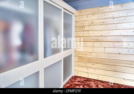 Elegant contemporary wardrobe with new clothes and matte glass on sliding door stands near wooden wall of comfortable house Stock Photo