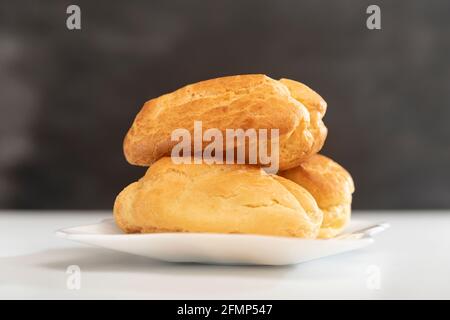 Profiteroles on white plate. Close up. Homemade puffs, popovers and eclairs. Side view. Stock Photo