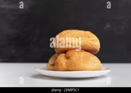 Profiteroles on white plate. Homemade puffs, popovers and eclairs. Side view. Stock Photo