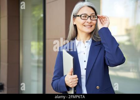 Joyous businesswoman adjusting her glasses while posing near office building Stock Photo