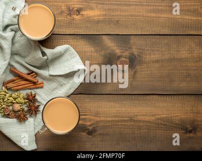 Two mugs with masala tea stand on a wooden table with spices. Top view. Copy space. Stock Photo