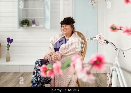 Attractive happy smiling middle aged woman sitting on wicker chair in backyard. Summer and spring vacations outside city, reuniting with nature. Stock Photo