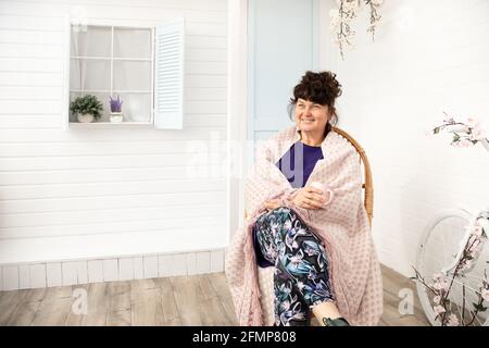 Attractive smiling middle aged woman sitting wicker chair in backyard.Summertime,springtime vacations outside city,reuniting with nature.copy space. Stock Photo