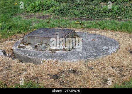 square metal manhole cover on a round concrete base surrounded by brown grass Stock Photo