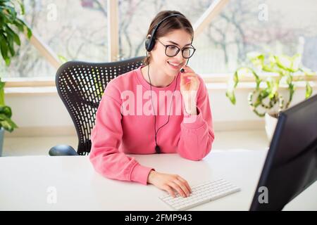 Customer service assistant wearing headset while sitting behind her computer and working from home. Home office. Stock Photo