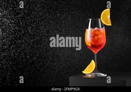 Aperol Spritz Cocktail in wine glass with splashing water on dark background. Long fizzy drink. Stock Photo