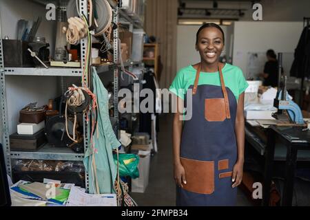Smiling young African female leather worker standing in her shop Stock Photo