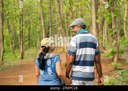 Backside portrait view of a middle aged couple holding hands, looking toward each other and smiling in a forest. Giving a romantic photo-shoot concept Stock Photo