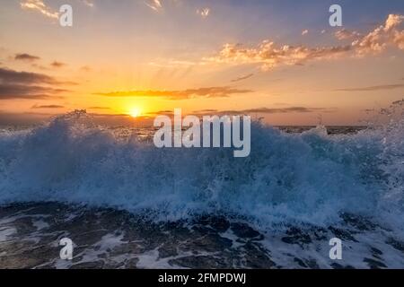 A Wave Is Breaking And Splashing As The Sun Sets On the Ocean Horizon Stock Photo
