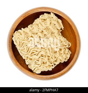 Dried instant noodles in a wooden bowl. Instant ramen are noodles sold in precooked and dried block form,  to be soaked in boiling water. Stock Photo