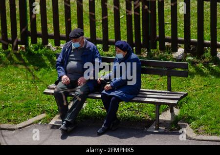 BRASOV, ROMANIA - 17 April 2021 - An elderly couple sit on a bench in Brasov, Romania. Despite an increasing amount of vaccinations, face masks are th Stock Photo