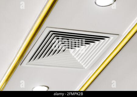 Square ventilation grill on the ceiling next to a spotlight. Stock Photo