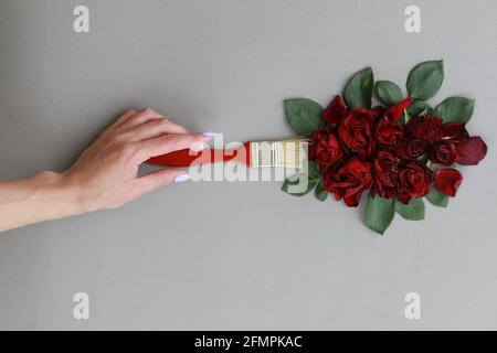 Creative layout with paint brush and red rose flowers on gray background. Woman hand hold brush paints. Copy space Stock Photo