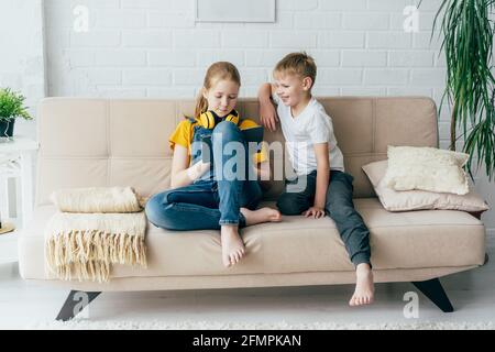 Friends teenagers sitting on the couch use a digital tablet to play. Children learn online. Stock Photo