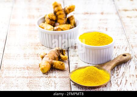 turmeric powder, saffron roots in wooden bowl on white table Stock Photo