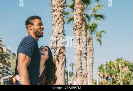 Young Interracial Couple Laughing Having Fun Together with Palm Trees Background at the Port (She Op Stock Photo