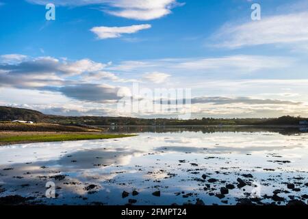 Tranquil scene with white clouds in blue sky reflected in calm sea at high tide in Red Wharf Bay, Isle of Anglesey, Wales, UK, Britain Stock Photo