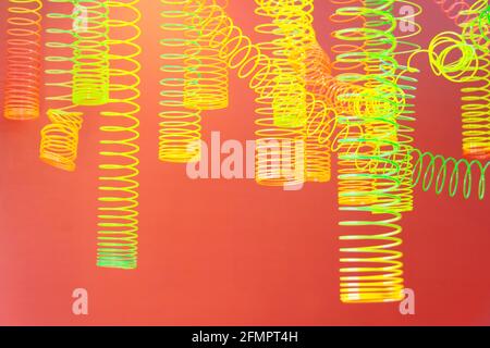 Abstract of rainbow spiral hanging colored toys, yellow light green on a red-orange background Stock Photo