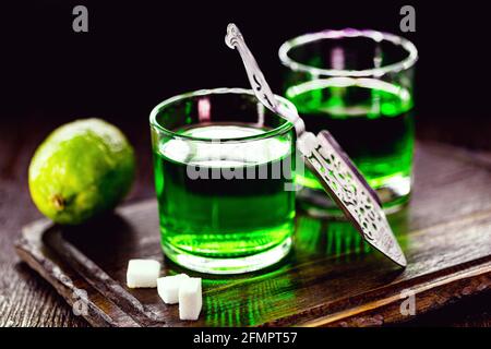 doses of absinthe with brown sugar cubes. distillate of absinthe in a glass and lemon, stainless steel spoon isolated on black background Stock Photo