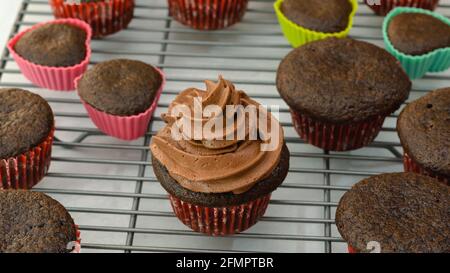 Frosting chocolate cupcakes with chocolate buttercream frosting, close up, woman hands, flat lay Stock Photo