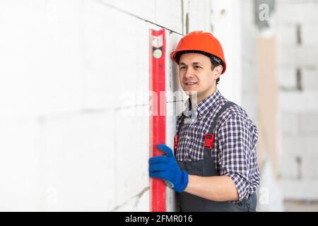 Young worker using water level meter measuring the wall builder working with autoclaved aerated concrete blocks. Walling, installing bricks in constru Stock Photo
