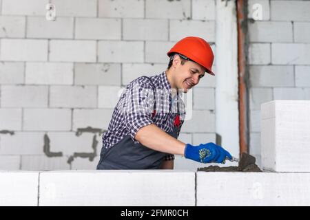 The process of bricklaying. Mason hands installing aerated concrete wall using special glue and tools necessary for brick works. Fresh mortar on aeroc Stock Photo