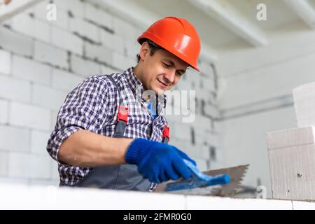 The process of bricklaying. Mason hands installing aerated concrete wall using special glue and tools necessary for brick works. Fresh mortar on aeroc Stock Photo