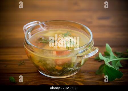fresh hot soup with chicken meatballs and vegetables in a plate on a wooden table Stock Photo