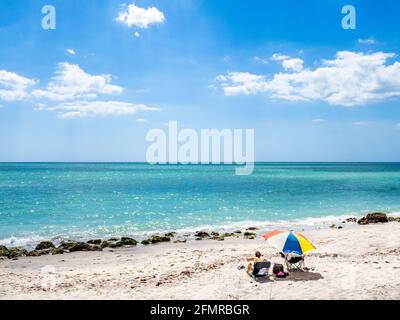 Couple relaxing on holiday under a beach umbrella on the Gulf of Mexico beach in Venice Florida USA Stock Photo