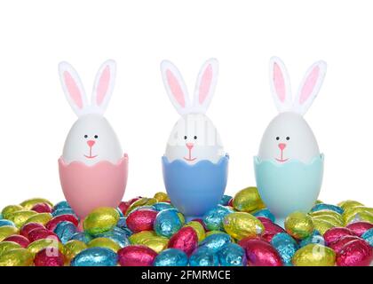 Row of Easter Eggs crafted into bunnies with felt ears, sitting in colorful egg cups with colorful foil wrapped chocolate egg candies, isolated on whi Stock Photo