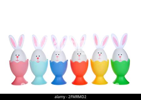 Row of Easter Eggs crafted into bunnies with felt ears, sitting in colorful egg cups isolated on white background. Stock Photo