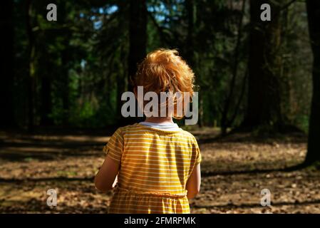 View of the back of a young girl with short ginger hair wearing a yellow dress with white stripes running horizontally across it. The girl is facing i Stock Photo