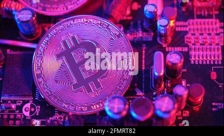 Cryptocurrency coins on circuit board. Bitcoins standing on CPU board. Close-up Bitcoin with blue and pink neon light. Printed circuit board with coin Stock Photo