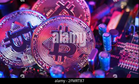 Cryptocurrency coins on circuit board. Bitcoins standing on CPU board. Close-up Bitcoin with blue and pink neon light. Printed circuit board with coin Stock Photo