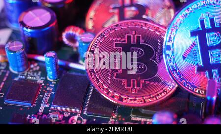 Cryptocurrency coins on circuit board. Bitcoins standing on CPU board. Close-up Bitcoin with blue and pink neon light. Printed circuit board with coin Stock Photo