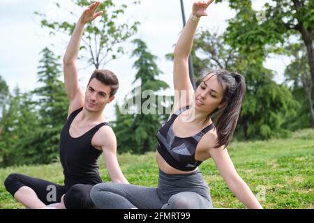 Young sporty couple stretching arms sitting on a mat in a park. Preparation for yoga exercises. Stock Photo
