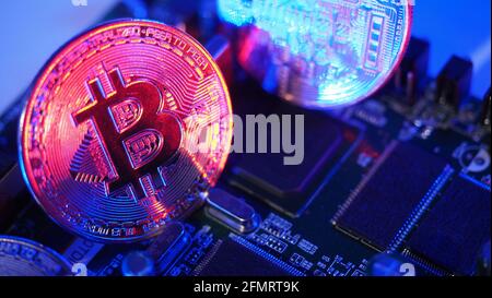 Cryptocurrency coins on circuit board. Bitcoins standing on CPU board. Close-up Bitcoin with blue and pink neon light. Printed circuit board with coin Stock Photo