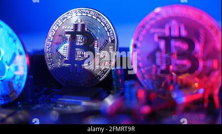 Cryptocurrency coins on circuit board. Bitcoins standing on CPU board. Close-up Bitcoin with blue and pink neon light. Printed circuit board with coin Stock Photo