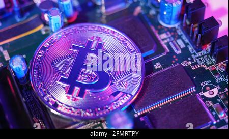 Cryptocurrency coins on circuit board. Bitcoins standing on CPU board. Close-up Bitcoin with blue and pink neon light. Printed circuit board with coin Stock Photo