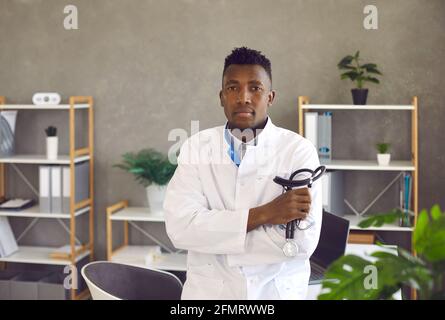 Young black doctor standing in medical office, holding stethoscope and looking at camera Stock Photo