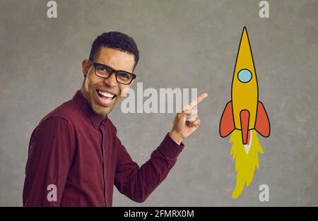 Portrait of a happy young black businessman pointing away at a flying cartoon rocket Stock Photo