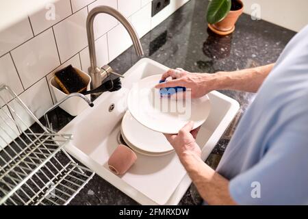 Cropped male hands washing dishes at kitchen sink while doing cleaning at home at weekends, Staying at home using free time about daily housekeeping r Stock Photo